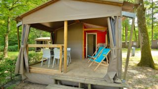 Photo of a Mobilodge cabin with a covered porch, deck chairs, dining set, and surrounded by forest trees.