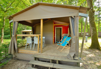 Foto di una cabina Mobilodge con veranda coperta, sedie a sdraio e tavolo, circondata da alberi verdi.