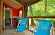 Knusse Mobilodge bij Camping Seasonova Etang de la Vallée in Frankrijk met blauwe ligstoelen en uitzicht op het bos.