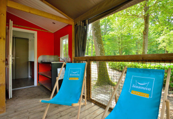Sfeervolle Mobilodge bij Camping Seasonova Etang de la Vallée in Frankrijk met blauwe strandstoelen en boszicht.