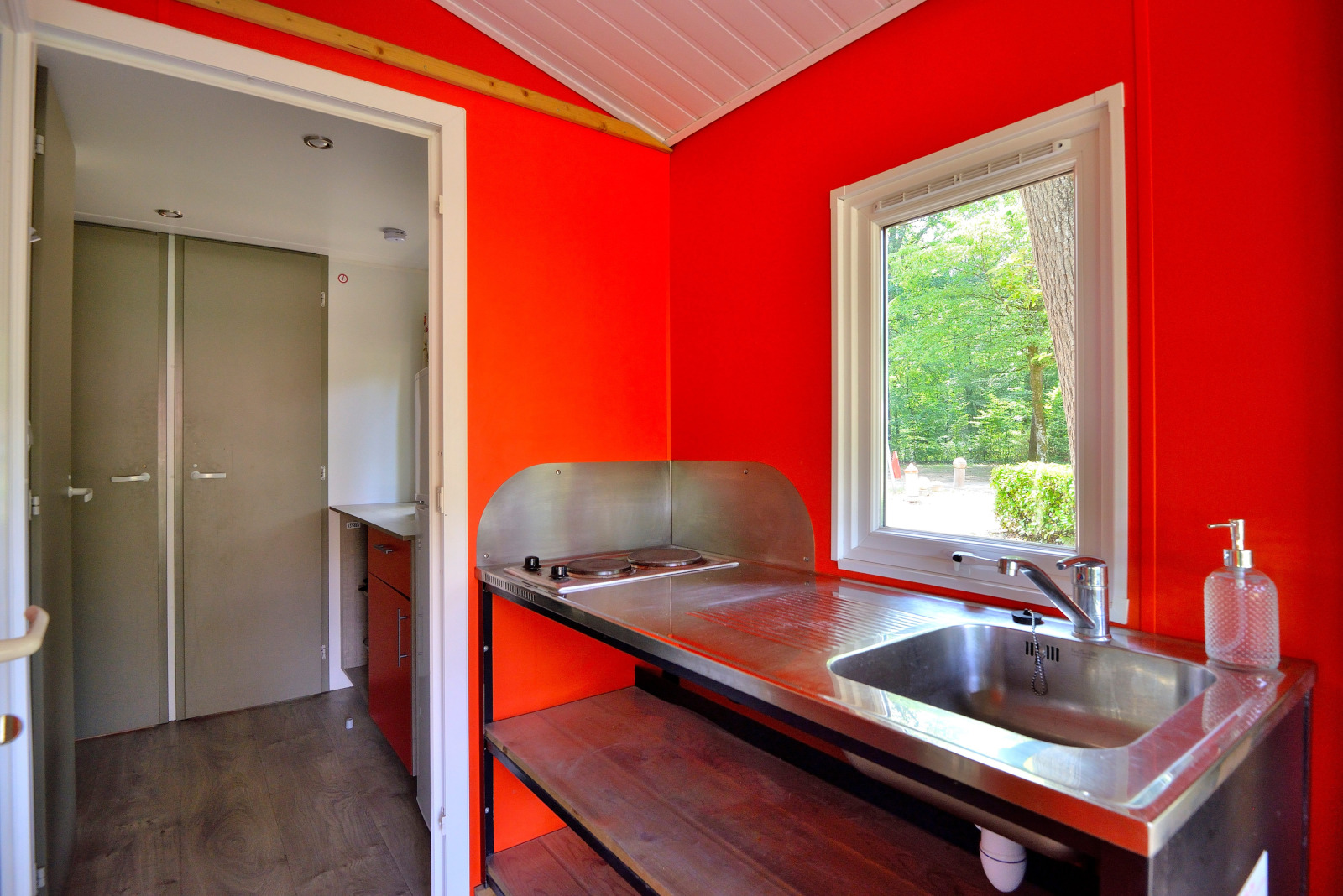 Keukeninterieur van een Mobilodge-hut op Camping Seasonova Etang de la Vallée met rode muur en raam.