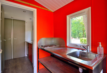 Innenansicht einer Mobilodge-Küche auf Camping Seasonova Etang de la Vallée mit roter Wand und Fenster.