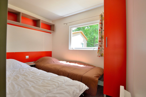 Helles Schlafzimmer mit zwei Einzelbetten in einer Mobilodge auf Camping Seasonova Etang de la Vallée, Frankreich.
