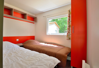 Helles Schlafzimmer mit zwei Einzelbetten in einer Mobilodge auf Camping Seasonova Etang de la Vallée, Frankreich.