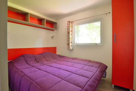 Dormitorio en Mobilodge de Camping Seasonova Etang de la Vallée, Francia, con edredón morado y ventana.