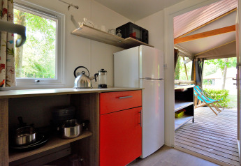 Compact Mobilodge kitchen with red cabinet, fridge, kettle, and terrace view at Camping Seasonova Etang de la Vallée.