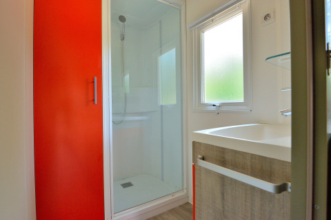 Baño moderno con puerta de armario roja, ducha, ventana y lavabo en Mobilodge en Camping Seasonova Etang de la Vallée, Francia.