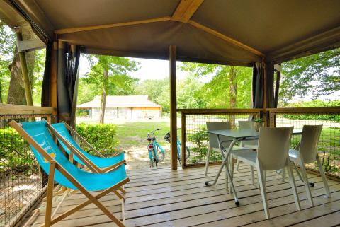 Veranda coperta Mobilodge al Camping Seasonova Etang de la Vallée con sdraio blu e tavolo con sedie.