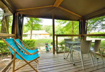 Overdekt terras van een Mobilodge op Camping Seasonova Etang de la Vallée, met stoelen en blauwe ligzetels.