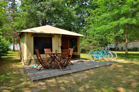 Safaritent Lodge Nature met houten terras, tuinset en twee turquoise fietsen tussen het groen in het bos.