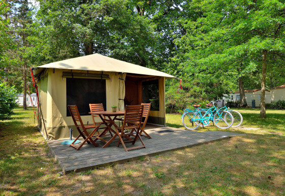 Safaritent Lodge Nature met houten terras, tuinset en twee turquoise fietsen tussen het groen in het bos.