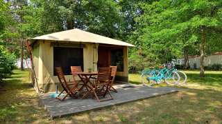 Tienda safari Lodge Nature con terraza de madera, muebles al aire libre y dos bicicletas turquesa en el bosque.