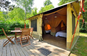 Safari-Lodgezelt mit hölzerner Terrasse und Gartenmöbeln bei Camping Seasonova Etang de la Vallée in Frankreich.