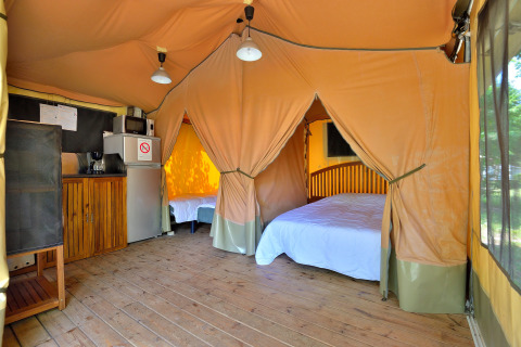 Interieur van een safari lodgetent met houten vloer, bedden en kitchenette op Camping Seasonova Etang de la Vallée.