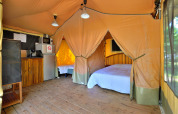 Interieur van een safari lodgetent met houten vloer, bedden en kitchenette bij Camping Seasonova Etang de la Vallée.
