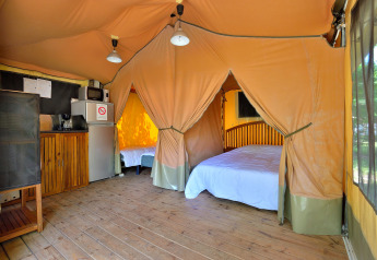 Interior de tienda safari tipo lodge con piso de madera, camas y cocina en Camping Seasonova Etang de la Vallée.