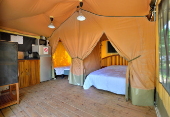 Interieur van een safari lodgetent met houten vloer, bedden en kitchenette op Camping Seasonova Etang de la Vallée.