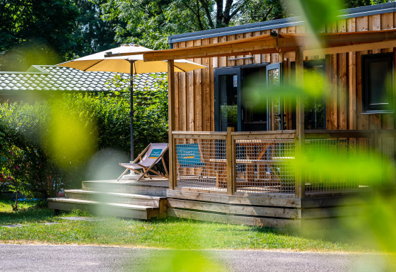 Glamping-Unterkunft mit Holzhaus, Terrasse, Liegestühlen und Sonnenschirm im Grünen gelegen.