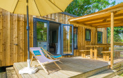 Moderne glampingverblijf met houten terras, ligzetel, parasol en overdekte picknickruimte buiten.