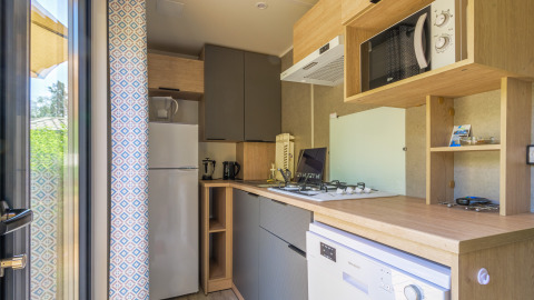 Cocina moderna en alojamiento glamping con estufa, microondas, nevera y lavavajillas integrados.