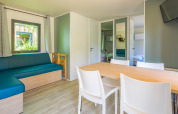 Alojamiento glamping moderno y luminoso con mesa de comedor, sillas blancas, sofá azul y televisor.