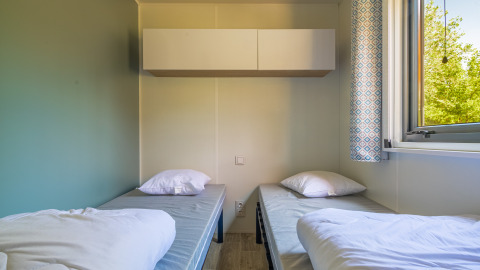 Twee aparte bedden met witte kussens in een glampingkamer, raam met zicht op groene bomen.