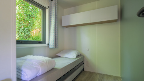 Helles, kompaktes Schlafzimmer mit Einzelbett und Fenster, das auf grüne Pflanzen im Glamping-Bereich blickt.