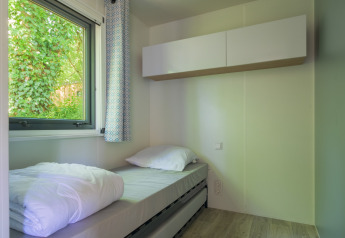 Dormitorio luminoso y compacto con cama individual y ventana con vistas a plantas verdes en un glamping.