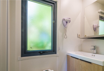 Badkamer in een glampingverblijf met mat raam, haardroger, spiegel en eigentijdse wastafel.