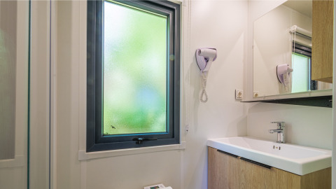 Badezimmer einer Glamping-Unterkunft mit mattem Fenster, Haartrockner, Spiegel und modernem Waschbecken.