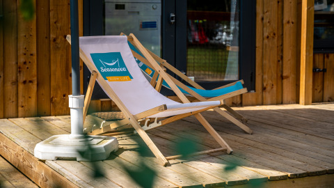 Twee ligzetels op een houten veranda voor een glampingtent, perfect om rustig te genieten van de natuur.