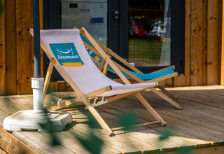 Twee ligzetels op een houten veranda voor een glampingtent, perfect om rustig te genieten van de natuur.