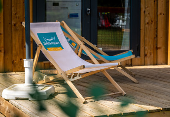 Two deck chairs sit on a wooden veranda outside a glamping cabin, ready for guests to relax in comfort.