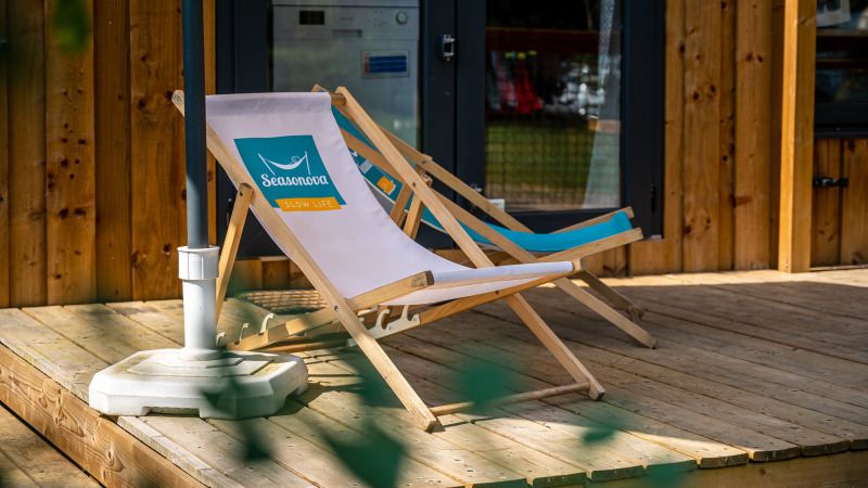 Dos tumbonas se encuentran en una terraza de madera frente a un alojamiento glamping, ideales para descansar.