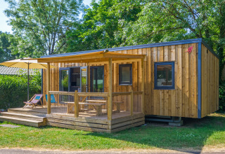 Moderne Glamping-Unterkunft aus Holz mit Terrasse, Sonnenschirm und Liegestühlen im Grünen.