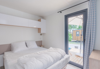 Lichte slaapkamer in het Cottage van Camping Seasonova Vesoul, Frankrijk, met deur naar een terras buiten.
