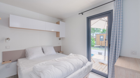 Dormitorio luminoso en la Cottage de Camping Seasonova Vesoul en Francia, con puerta a terraza y decoración sencilla.