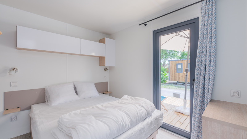 Dormitorio luminoso en la Cottage de Camping Seasonova Vesoul en Francia, con puerta a terraza y decoración sencilla.