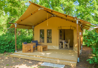Safari tent at Slow Lodge with wooden deck, outdoor seating, and surrounded by lush green trees.