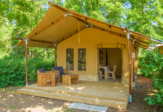 Safari tent at Slow Lodge with wooden deck, outdoor seating, and surrounded by lush green trees.