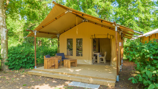 Safari tent at Slow Lodge with wooden deck, outdoor seating, and surrounded by lush green trees.