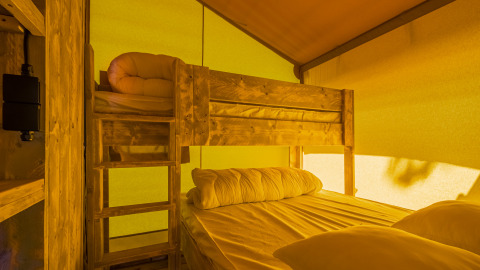 Slaapkamer in een safaritent met een houten stapelbed en door zonlicht geelgekleurde wanden.