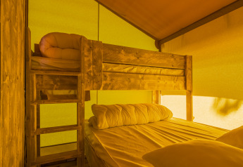 Interieur van een safaritent slaapkamer met houten stapelbed en geel verlichte canvas wanden.