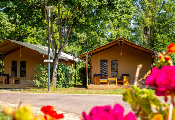 Safaritenten bij Slow Lodge op Camping Seasonova Vesoul in Frankrijk, omringd door bomen en kleurrijke bloemen.