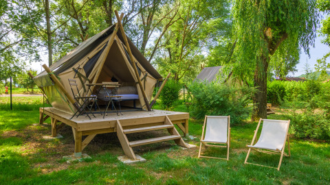 Tipitent op een houten terras in een groene tuin, met tafel, stoelen en twee relaxstoelen aan de voorkant.