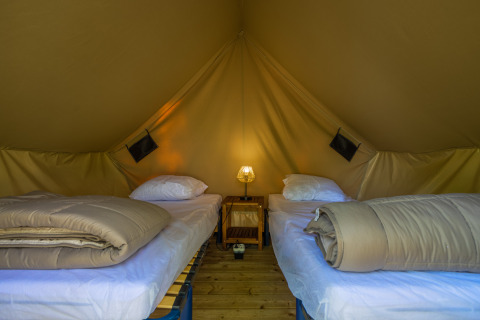 Binnenin een tipi tent met twee eenpersoonsbedden, dekbedden en een lampje op een nachtkastje.