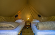Binnenin een tipi tent met twee eenpersoonsbedden, dekbedden en een lampje op een nachtkastje.