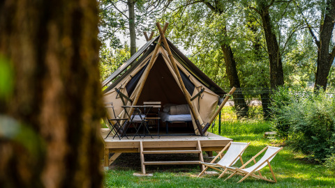 Tipi tent op een houten platform in een bos, met strandstoelen en een tafeltje vooraan op het gras.