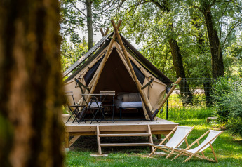 Tenda tipì su piattaforma di legno in una foresta verde, con sedie e tavolo all'aperto davanti.