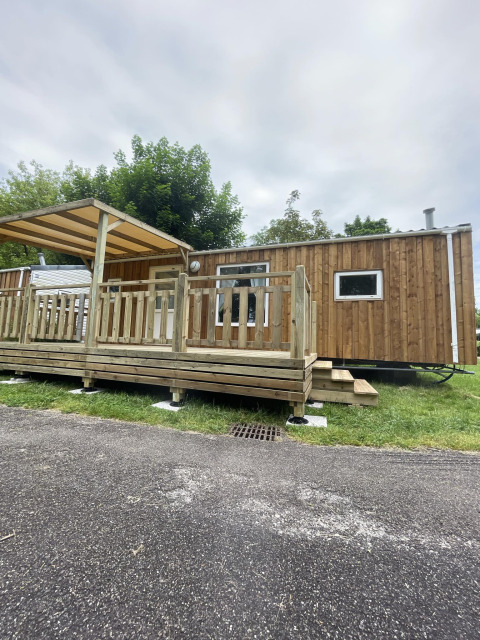 Außenansicht von Cottage Zen, einer Holzhütte mit Veranda und Dach auf einer grünen Wiese.